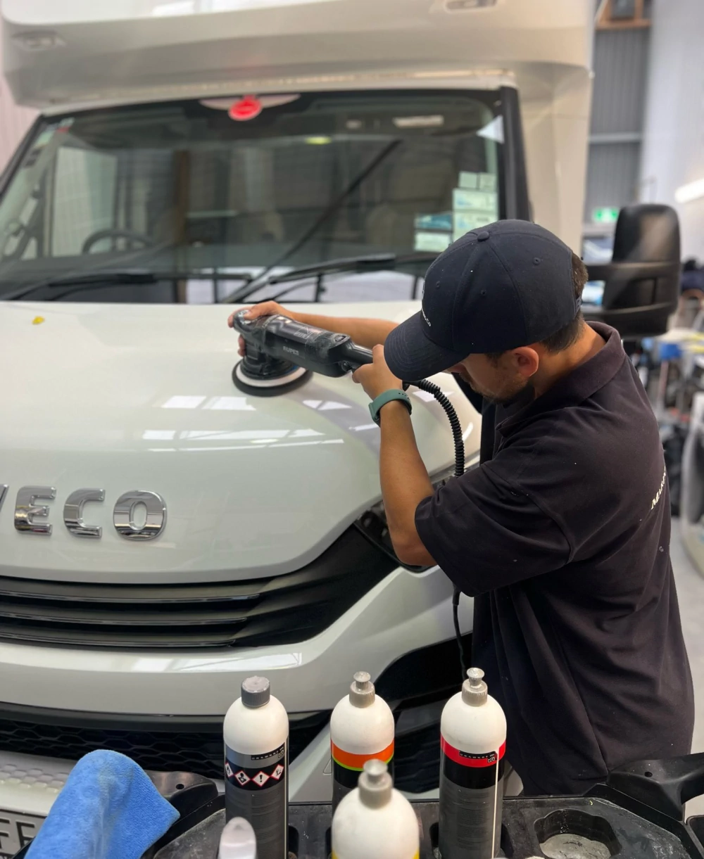 Technician machine-polishing a white Iveco motorhome bonnet