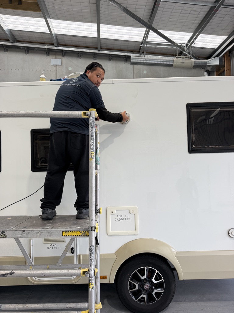 Detailer on scaffolding machine-polishing the sidewall of a motorhome inside the workshop